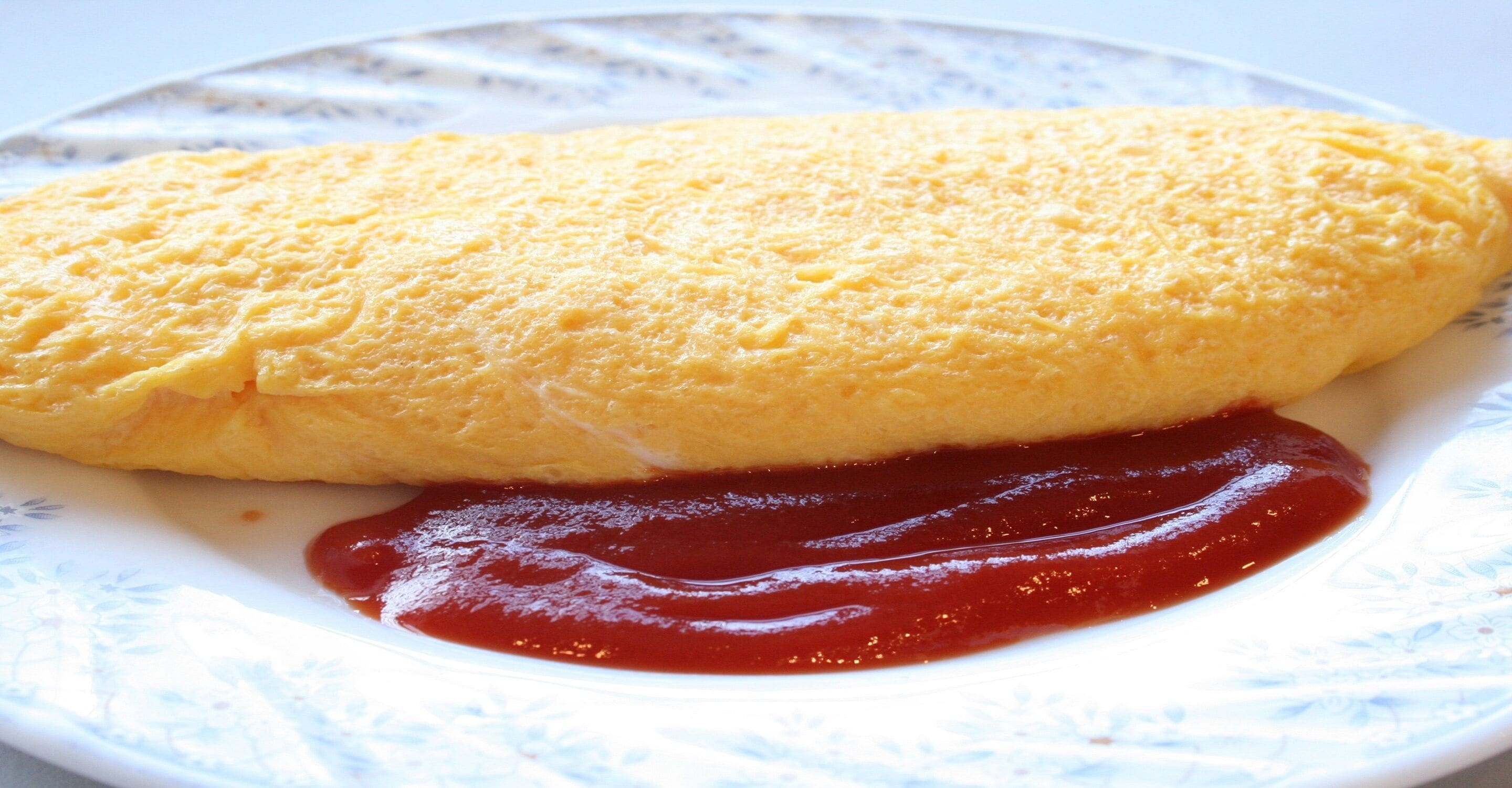 A plate with a folded omelette and a dollop of ketchup.