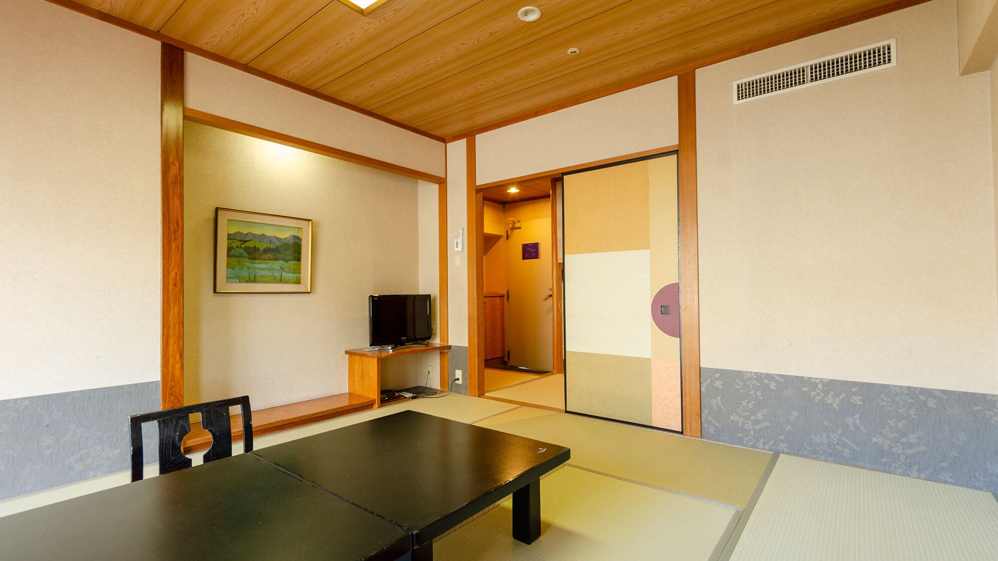 Une pièce de style japonais traditionnel, avec un sol recouvert de tatamis, une petite table basse, un téléviseur et une porte coulissante donnant sur une autre pièce.