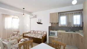En kompakt opholdsstue med sofa, spisebord, stole, et tekøkken og en loftlampe.