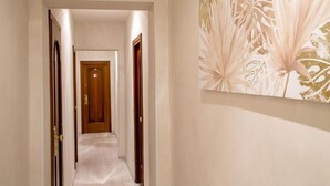 A hallway with a wooden door at the end, a light-colored carpet, and a wall with a floral pattern. - Amalia Suites (Rome)