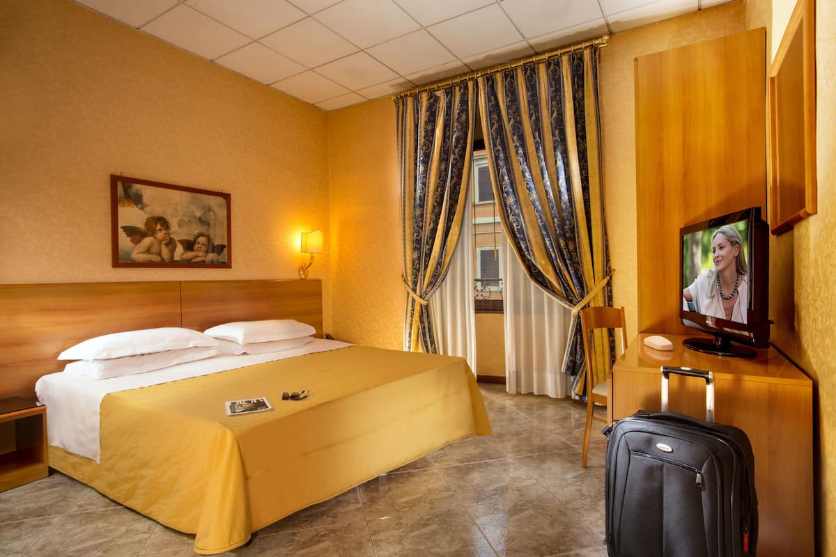 A hotel room with a bed, a television, a suitcase, and a painting on the wall.