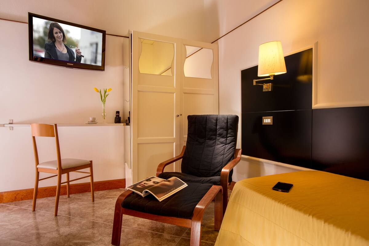 A hotel room with a bed, a chair, a desk, a TV, and a lamp.