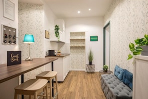 A hotel room with a wooden bar, a sofa, and a small table with a lamp. - Amalia Suites (Rome)