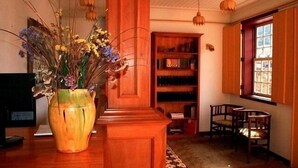 Una habitación con una estantería de madera, un jarrón grande con flores secas y dos sillas.