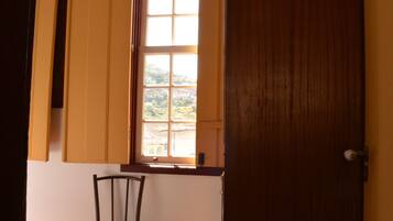 Una habitación con suelo de madera, una ventana con contraventanas amarillas y una puerta de madera.