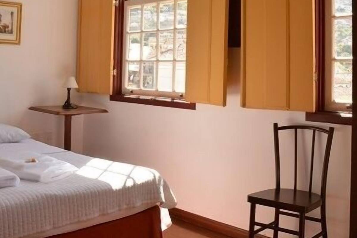 A bedroom with a bed, a chair, a table, and a window with curtains.