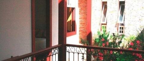 A balcony with a wrought iron railing, a brick wall, and a window with a white blind.
