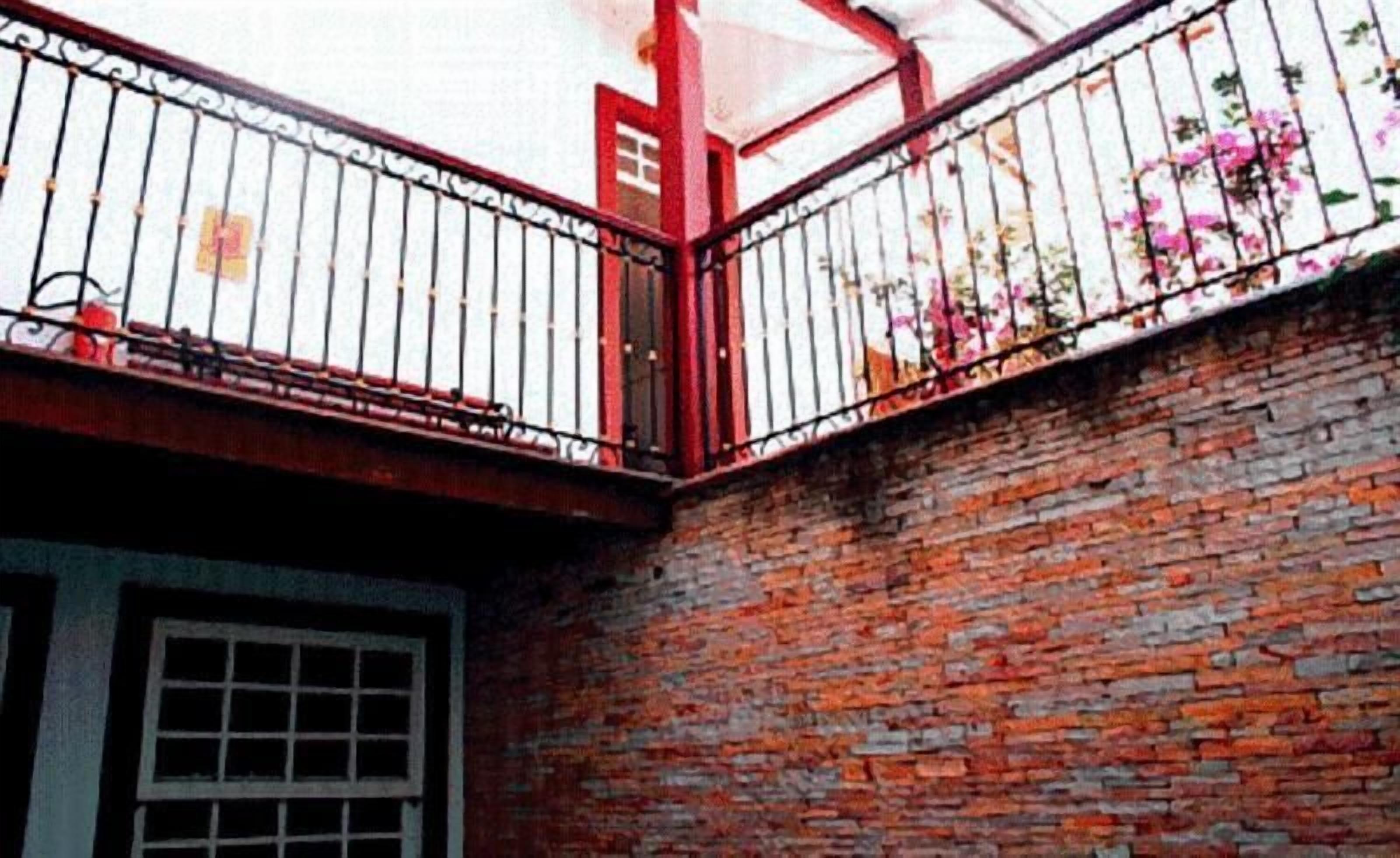 Un bâtiment en briques avec une rambarde métallique rouge et une fenêtre.