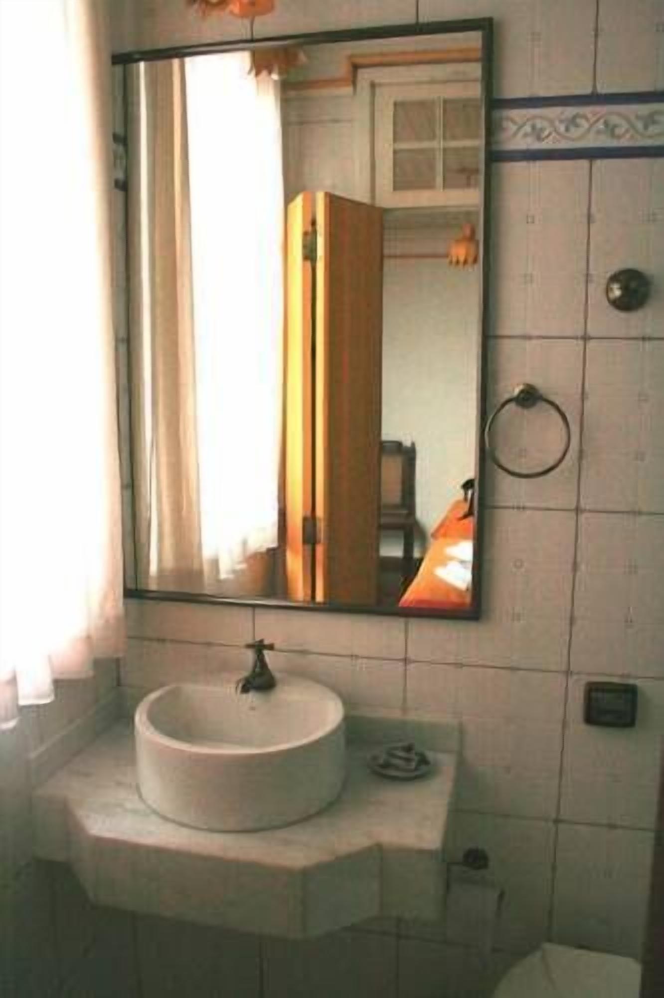 Un baño con un lavamanos redondo, un espejo y un perchero para toallas.