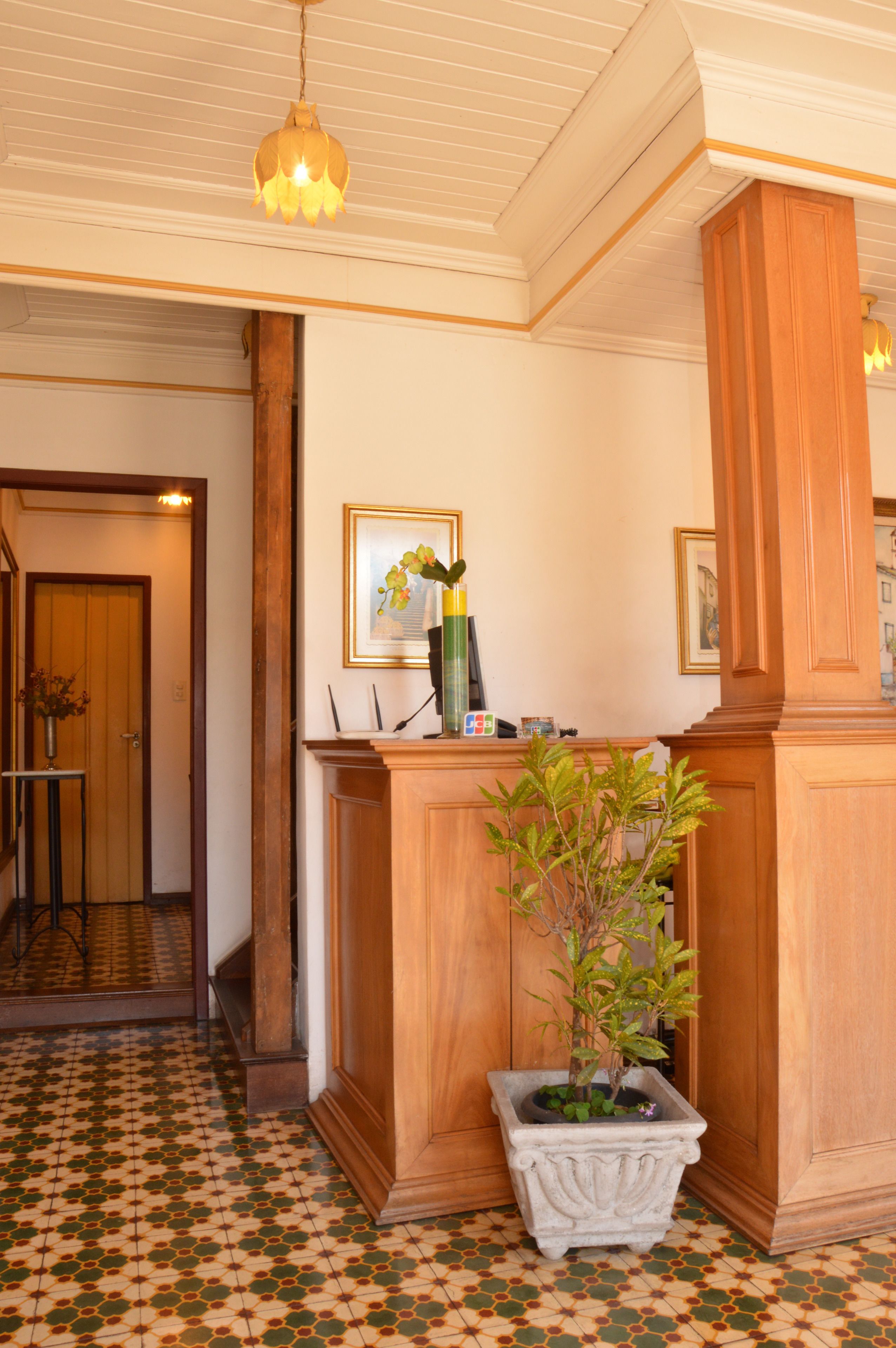 A reception area with a wooden reception desk, a potted plant, framed artwork, and a patterned floor.