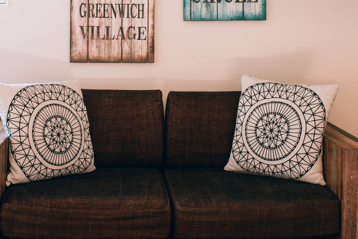 A wooden sign with text and a brown couch with patterned pillows.