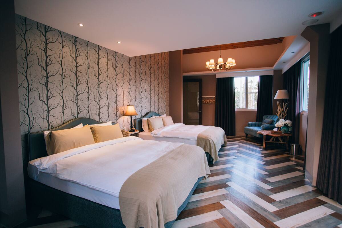 A hotel room with two beds, a wooden floor, a chandelier, and a view of the outdoors.