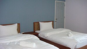 Une chambre d’hôtel avec deux lits simples, des têtes de lit en bois, du linge de lit blanc et une porte fermée.