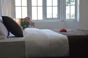 Un letto rifatto con lenzuola bianche e marroni, un vaso di fiori e una finestra con vista su un paesaggio verde.
