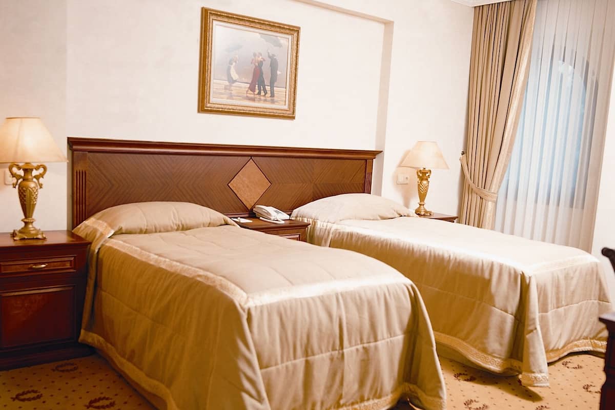 Habitació d'hotel amb dos llits, un panell de capçalera de fusta, un quadre a la paret i una finestra amb cortines.