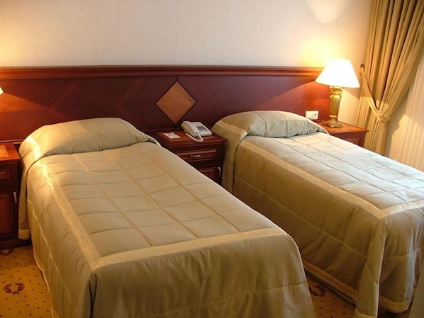 Una habitación de hotel con dos camas individuales, un cabecero de madera, una mesita de noche con lámpara y un teléfono.