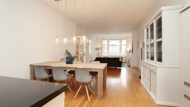 Een moderne keuken met een houten eettafel, grijze stoelen en hanglampen.