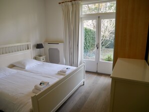Een hotelkamer met een tweepersoonsbed, een nachtkastje met een lamp, een radiator en uitzicht op de tuin door een glazen deur.