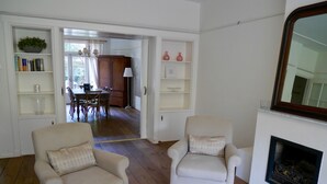 Een woonkamer met twee fauteuils, een open haard, en een eethoek die door een open doorgang zichtbaar is.
