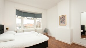 Een slaapkamer met een groot bed, een raam met uitzicht, een stoel en een ingelijst schilderij aan de muur.