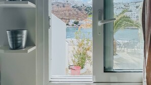 Un bagno con una finestra vista su una città costiera, un lavandino e secchi di metallo su mensole.