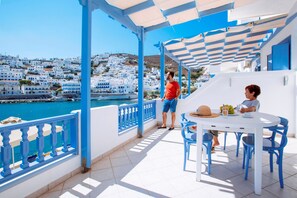 A terrace with a white table and blue chairs, overlooking a coastal town with white buildings. - Vithos Aparthotel (Astypalaia)