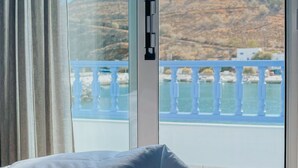 Una stanza con un letto e un'ampia finestra vista sulla costa, con ringhiera bianca e edifici.