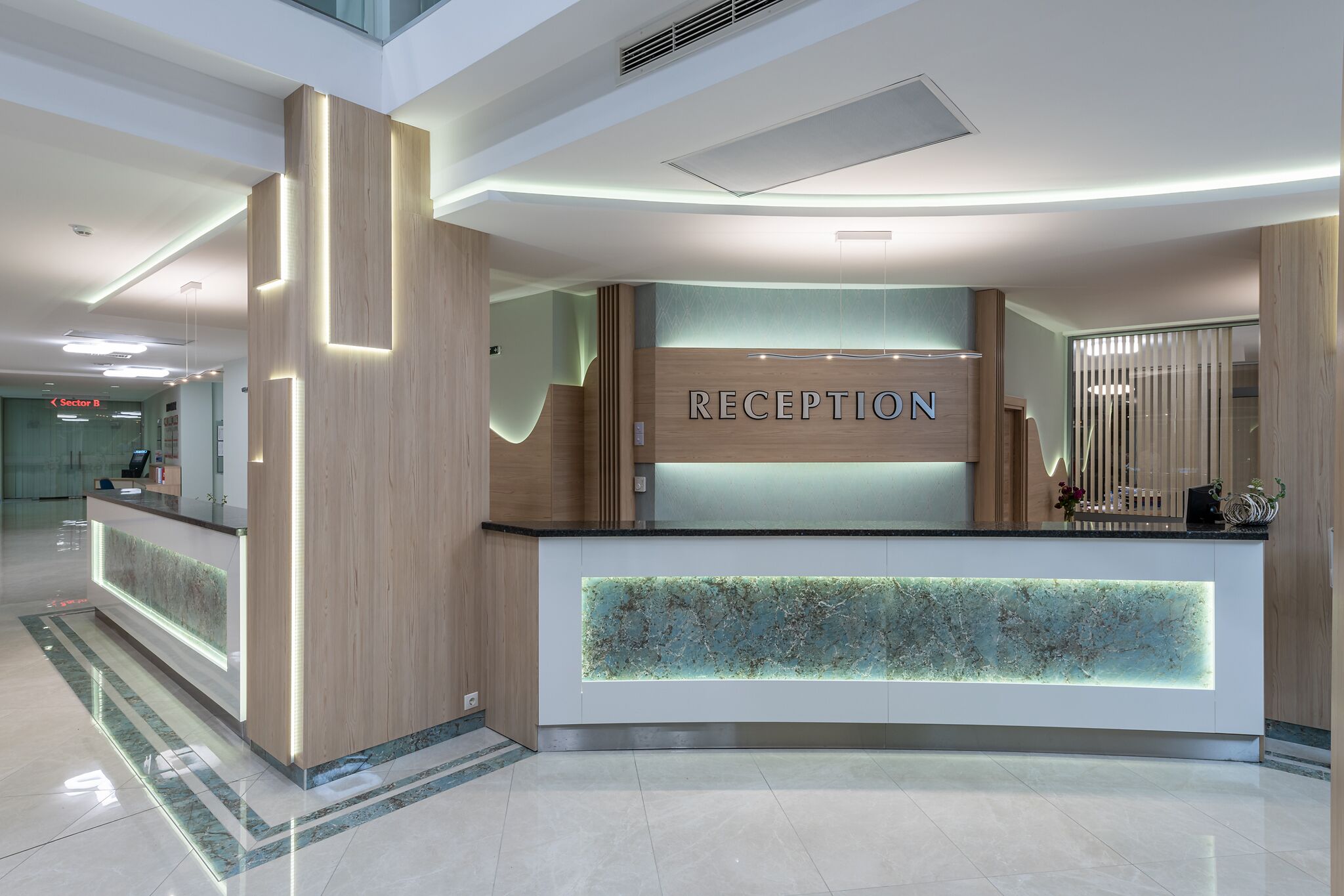 A modern reception desk with a 'RECEPTION' sign, a glass panel, and a wooden accent wall.