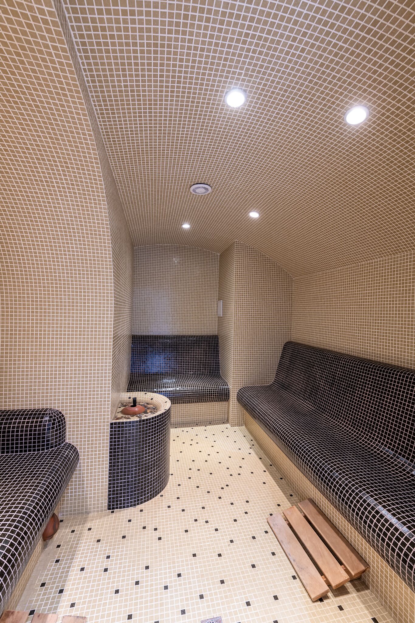 Un cuarto de spa con paredes y suelo de baldosas, una zona de estar circular y dos sofás.