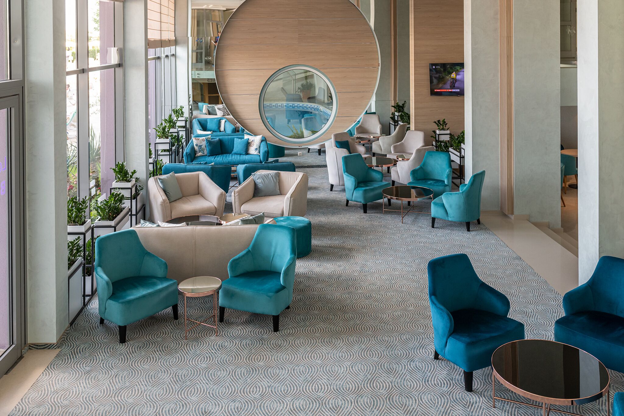 A spacious lobby with teal and white furniture, a large circular window, and a patterned carpet.