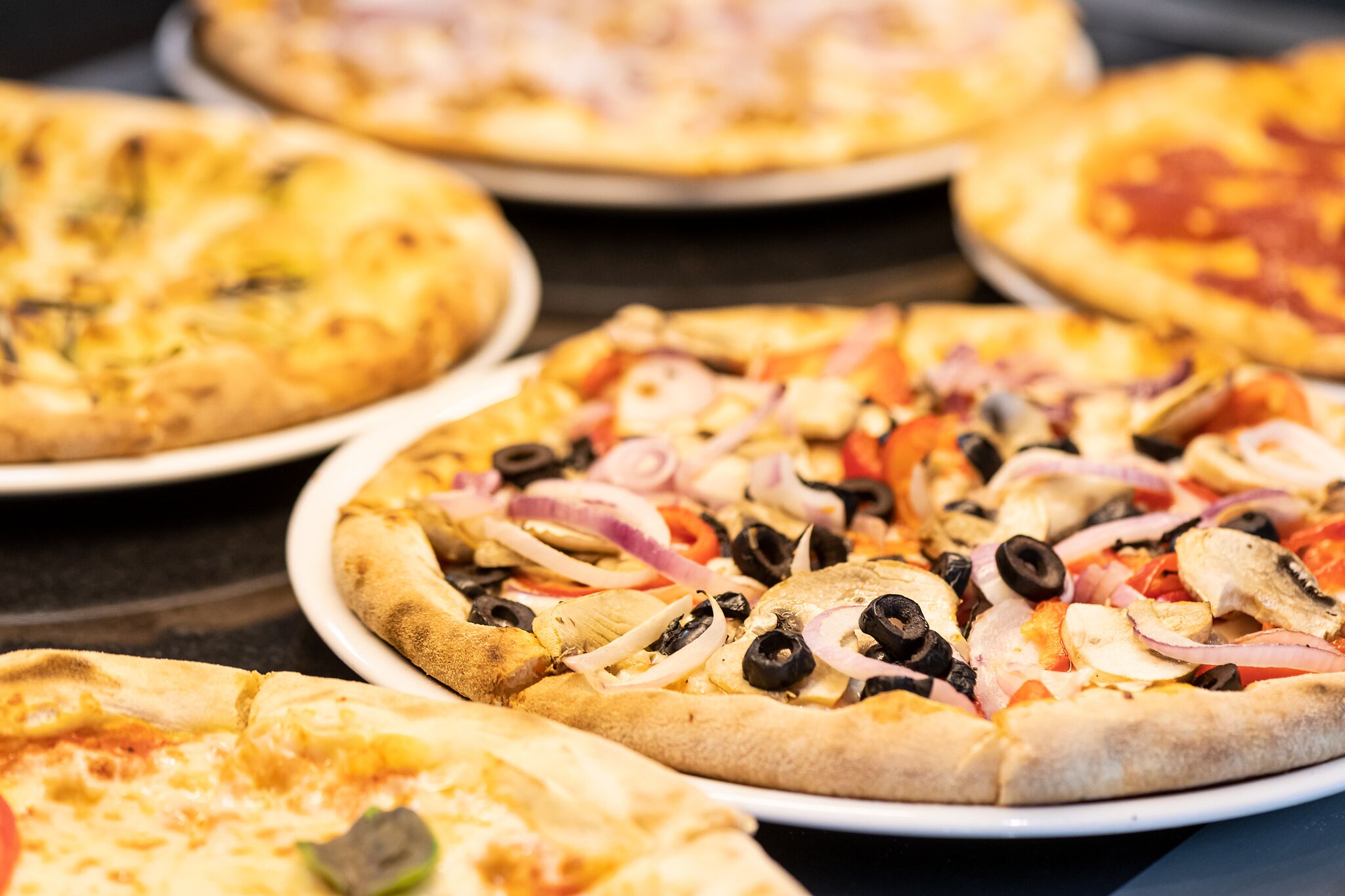 A variety of pizzas with different toppings on white plates.