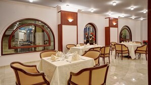 Un comedor con mesas redondas, sillas y ventanas arqueadas grandes.