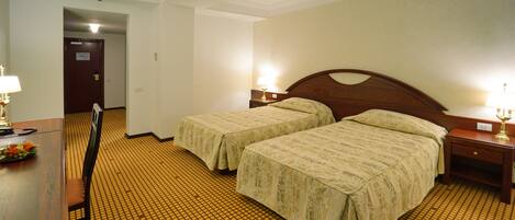 A hotel room with two beds, a desk, and a chair.