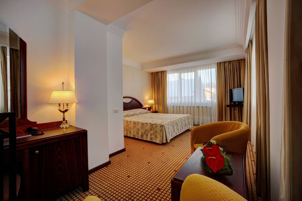 A hotel room with a bed, a desk with a lamp, a chair, and a television.