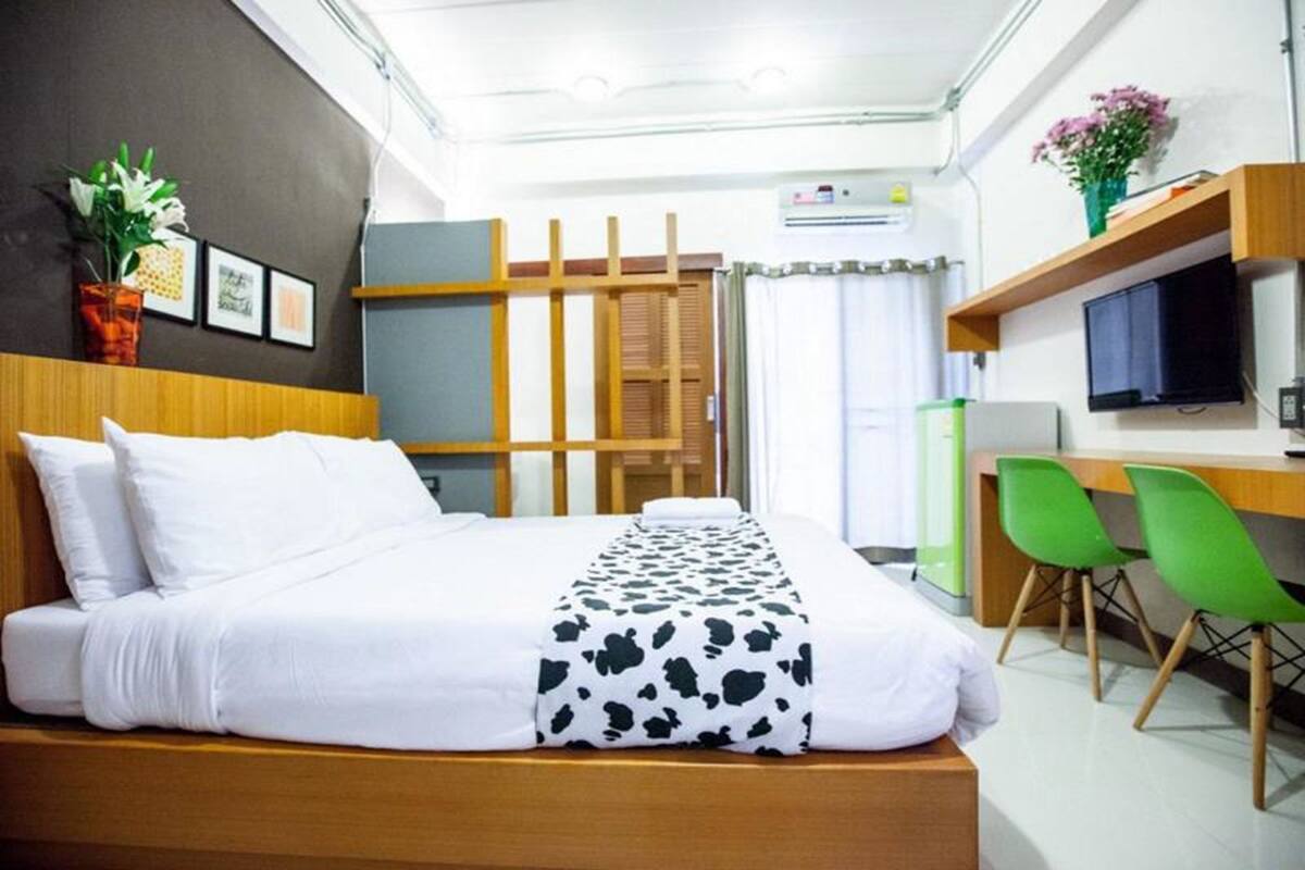Una habitación de hotel con cama, escritorio, silla, televisor y planta.