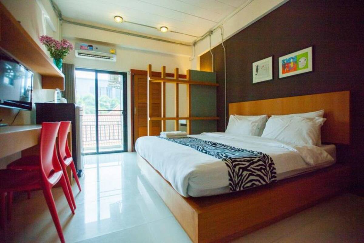 Una habitación de hotel con cama, escritorio con silla, televisor y puerta corrediza al exterior.