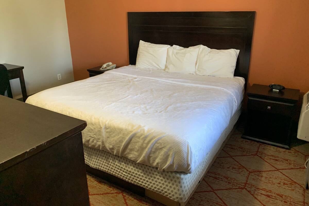 A neatly made bed with white bedding, a dark headboard, and a bedside table with a phone and a small object.