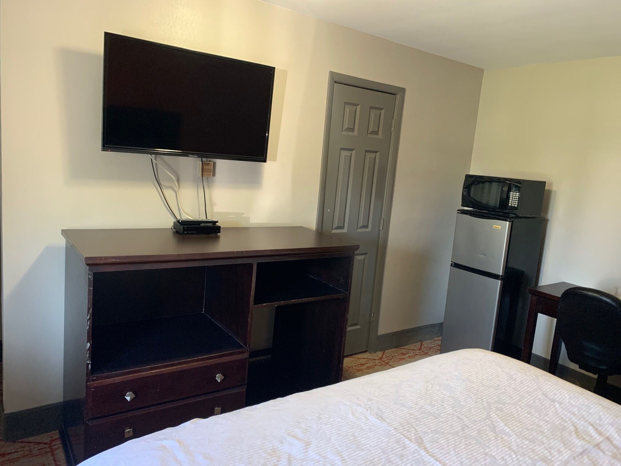 A hotel room with a bed, a TV mounted on a dresser, a refrigerator, and a microwave.