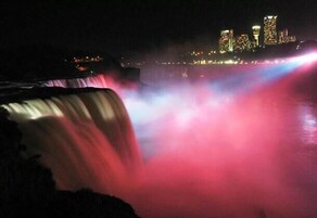 Vista noturna de uma cachoeira com edifícios iluminados ao fundo.
