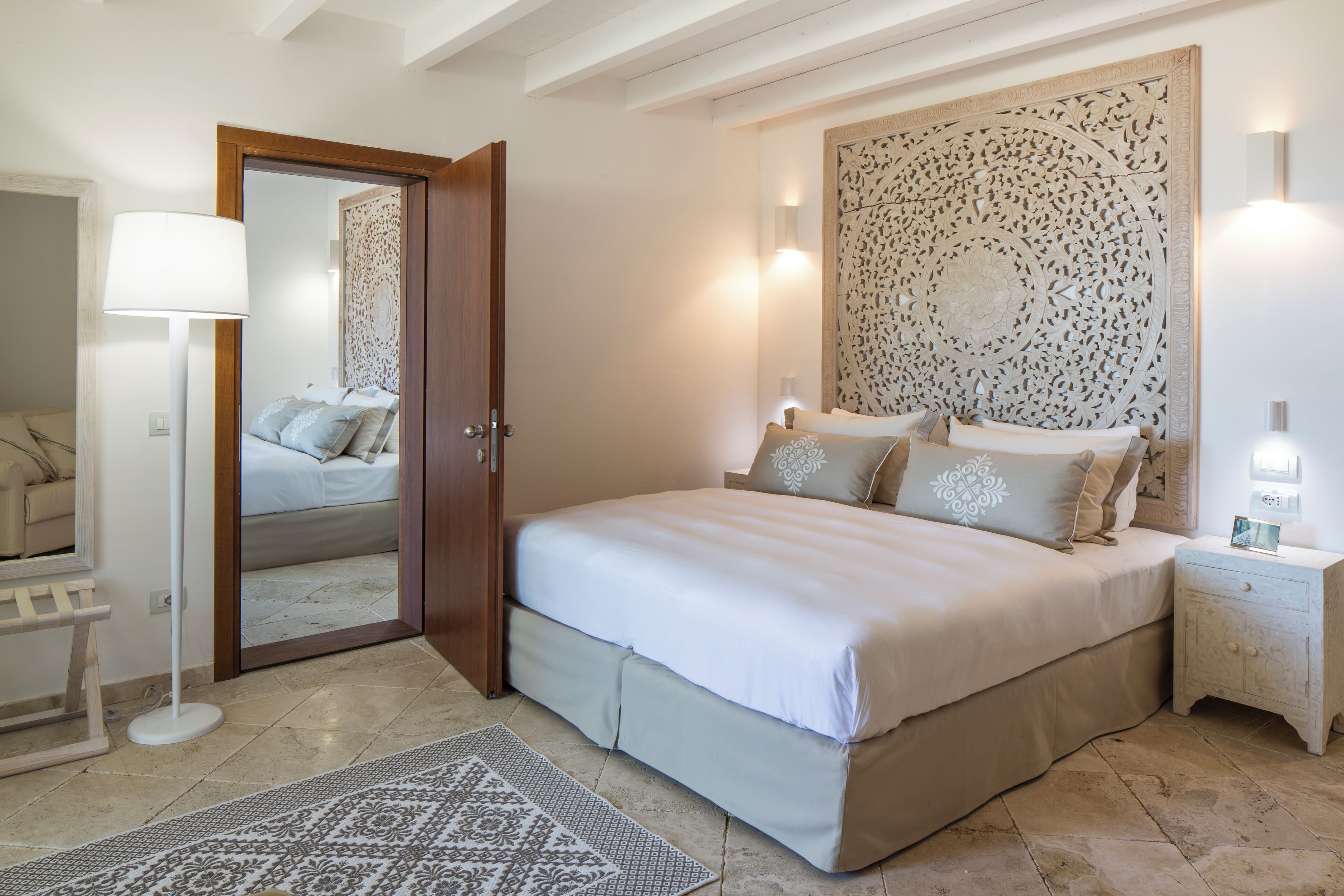 A bedroom with a large bed, bedside tables, a mirror, and a decorative wall panel.