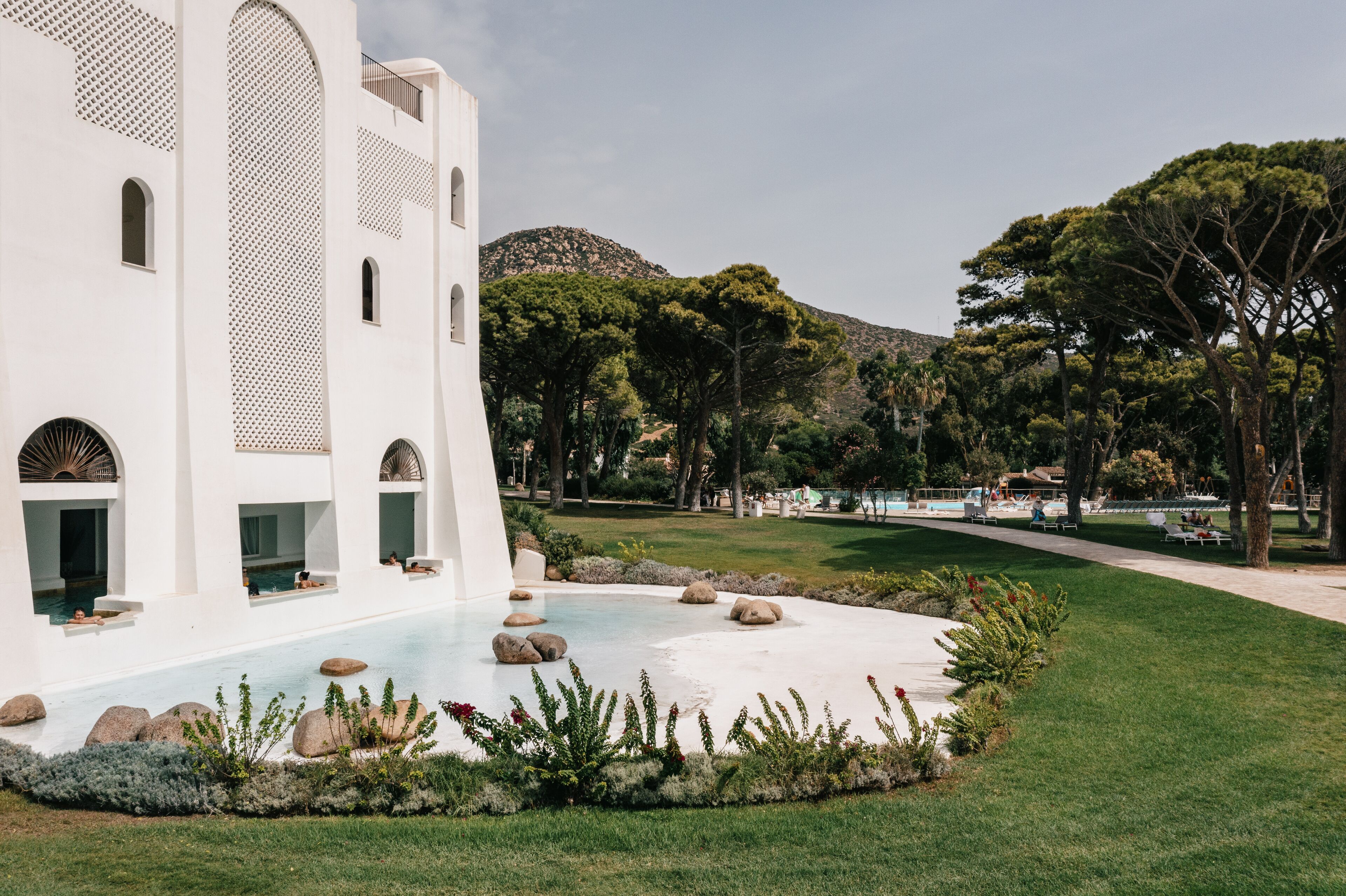 A white building with arched windows and a pool area with rocks and plants.