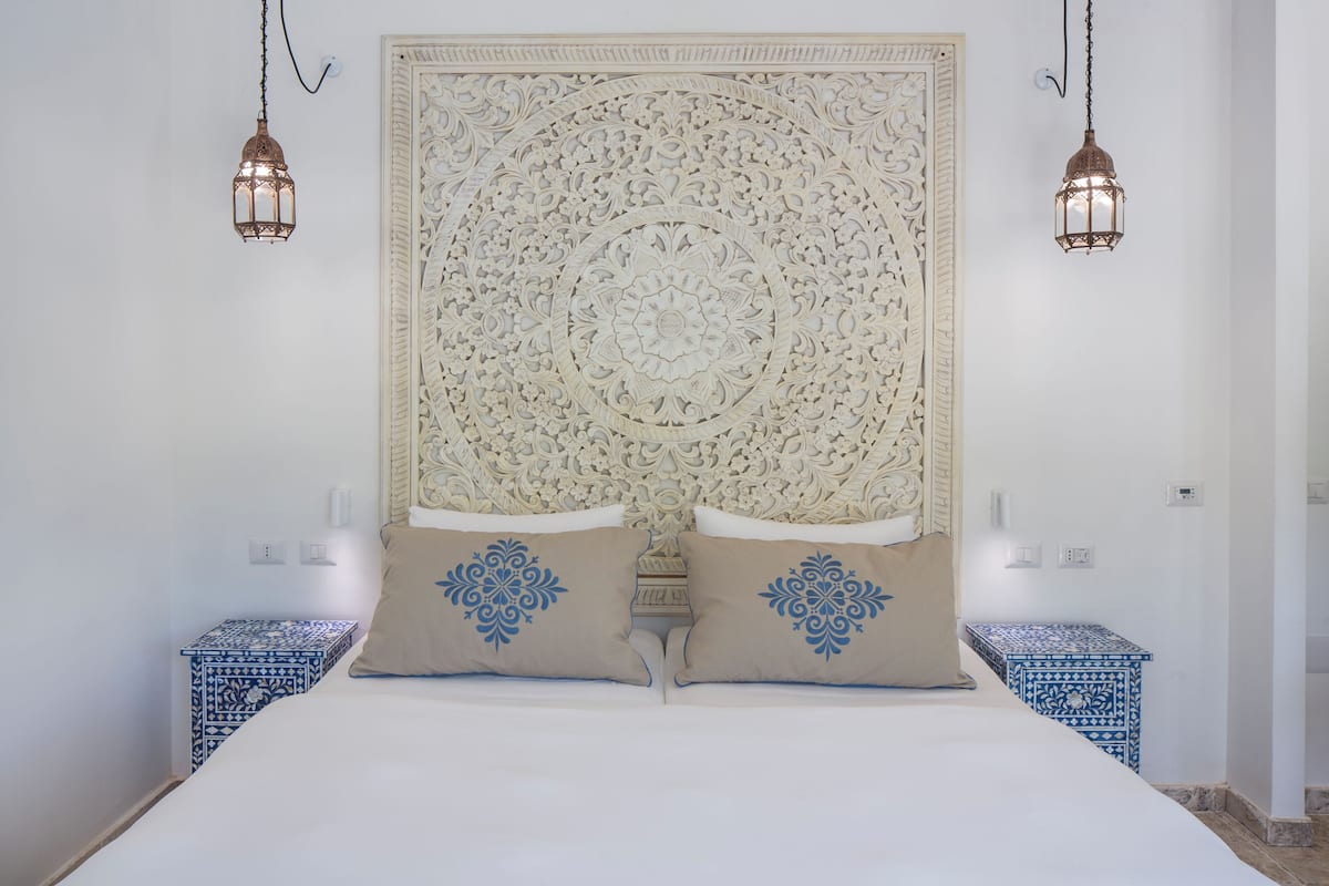 A bed with a decorative headboard, two matching pillows, and two hanging lanterns.
