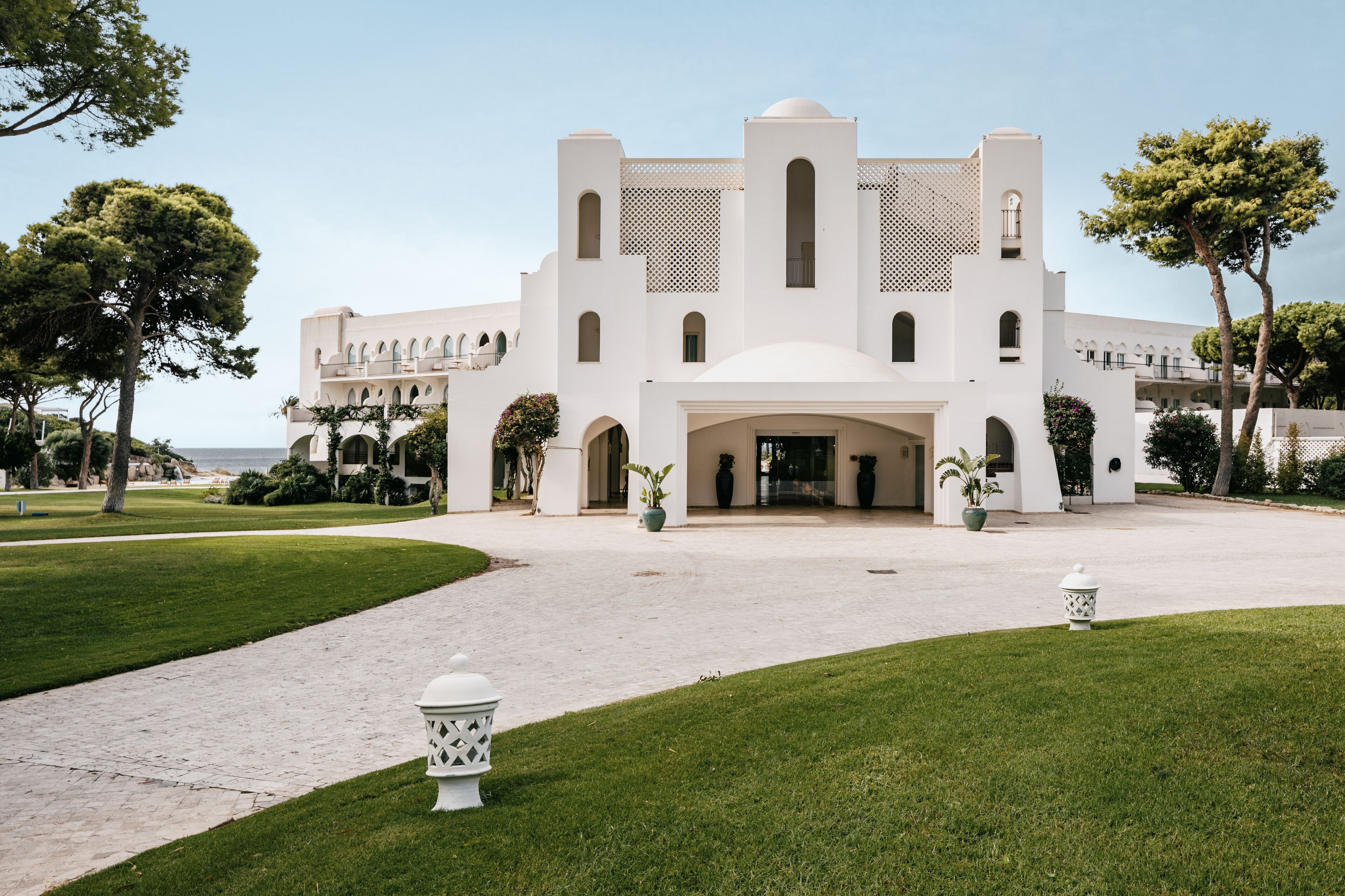 A white building with arched windows and a central dome, surrounded by a well-manicured lawn and trees.