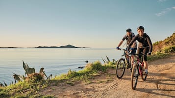 Dos ciclistas en un sendero de tierra junto a un lago con una montaña distante.