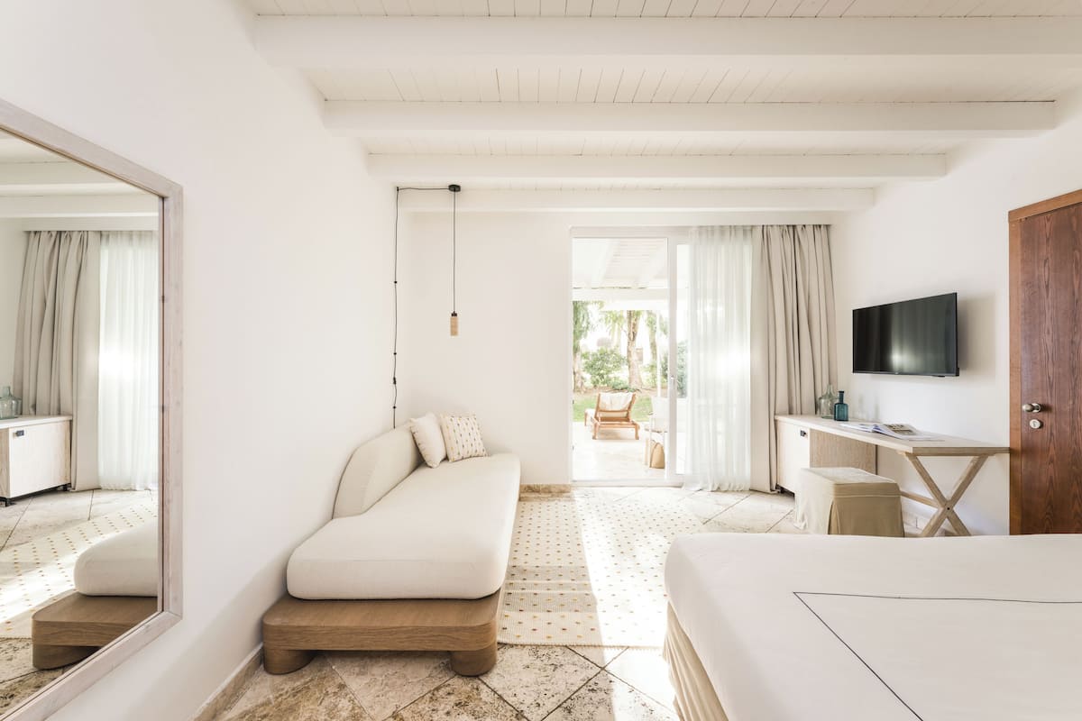 A bedroom with a bed, a desk, a television, and a view of the outdoors.