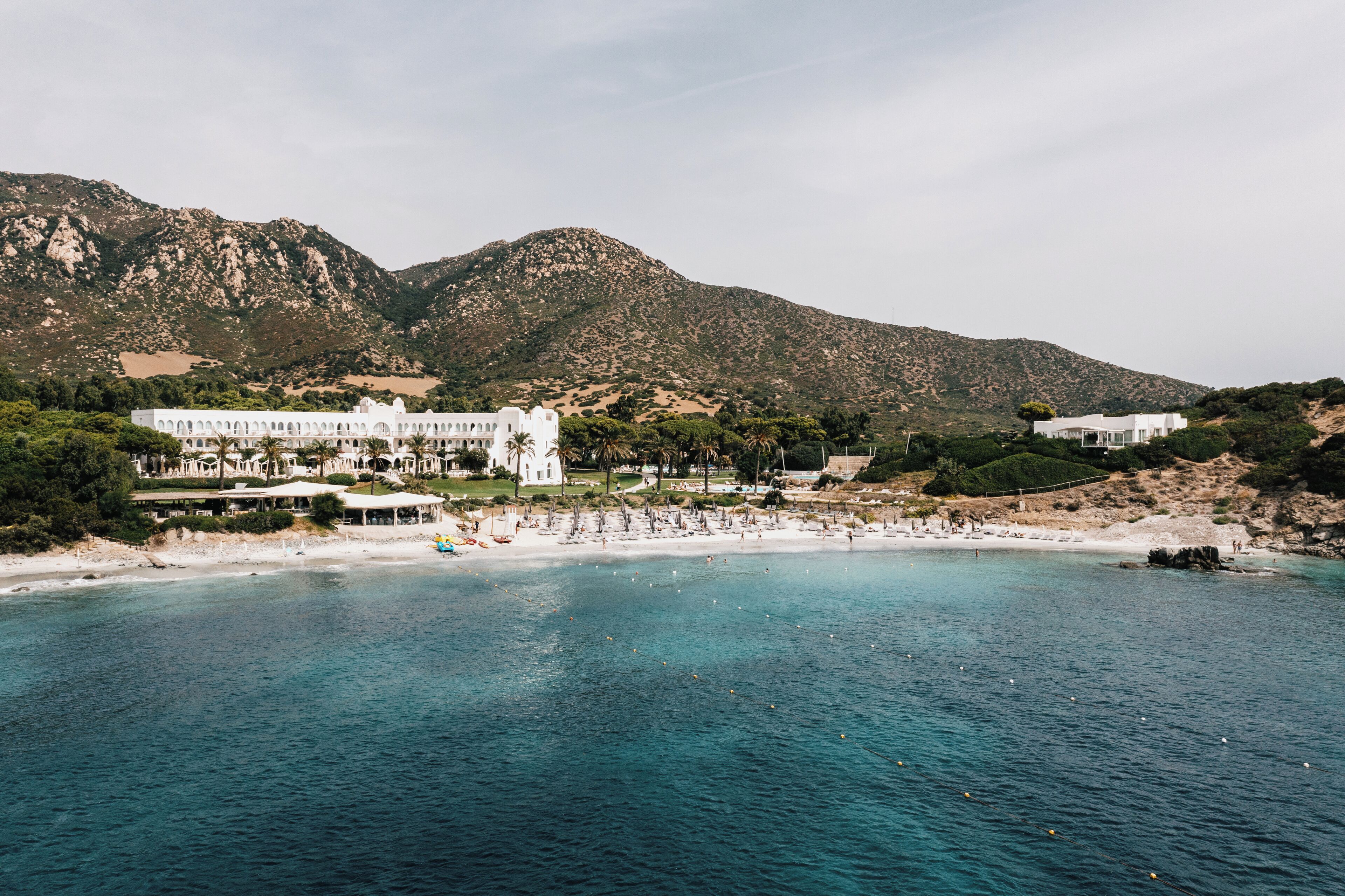 A coastal resort with a beach, white buildings, and mountains in the background.