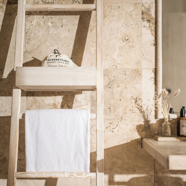 A wooden ladder with a white towel and a bag labeled 'Falkensteiner Resort Cabo Boj Premium Collection' against a marble wall.