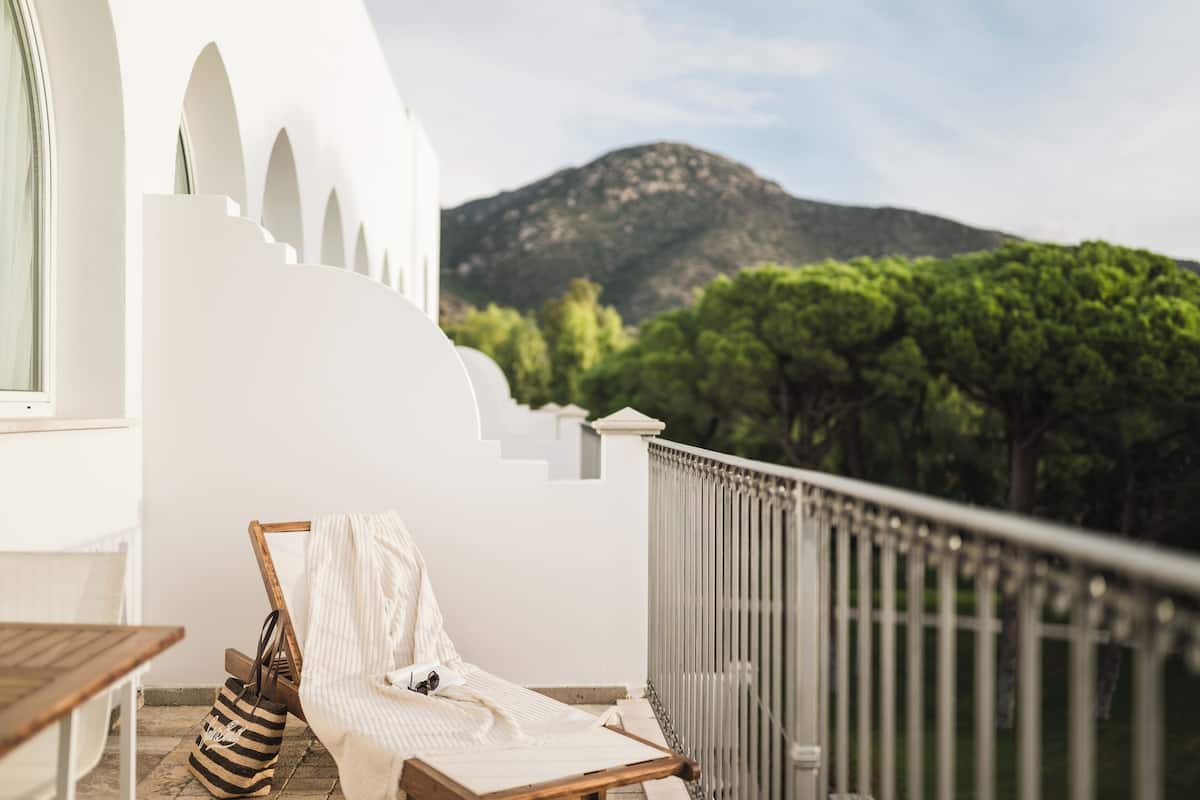 A balcony with a white chair, a striped bag, and a wooden table.