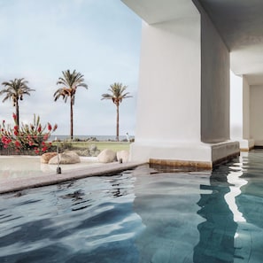 An infinity pool with clear water, palm trees, and a view of the ocean. - Falkensteiner Resort Capo Boi (Villasimius)