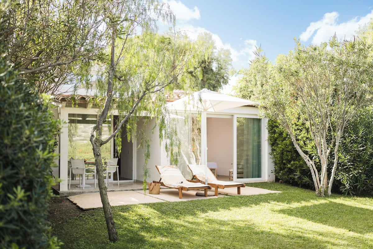 A modern house with a glass door leading to a patio area with two lounge chairs and a table.